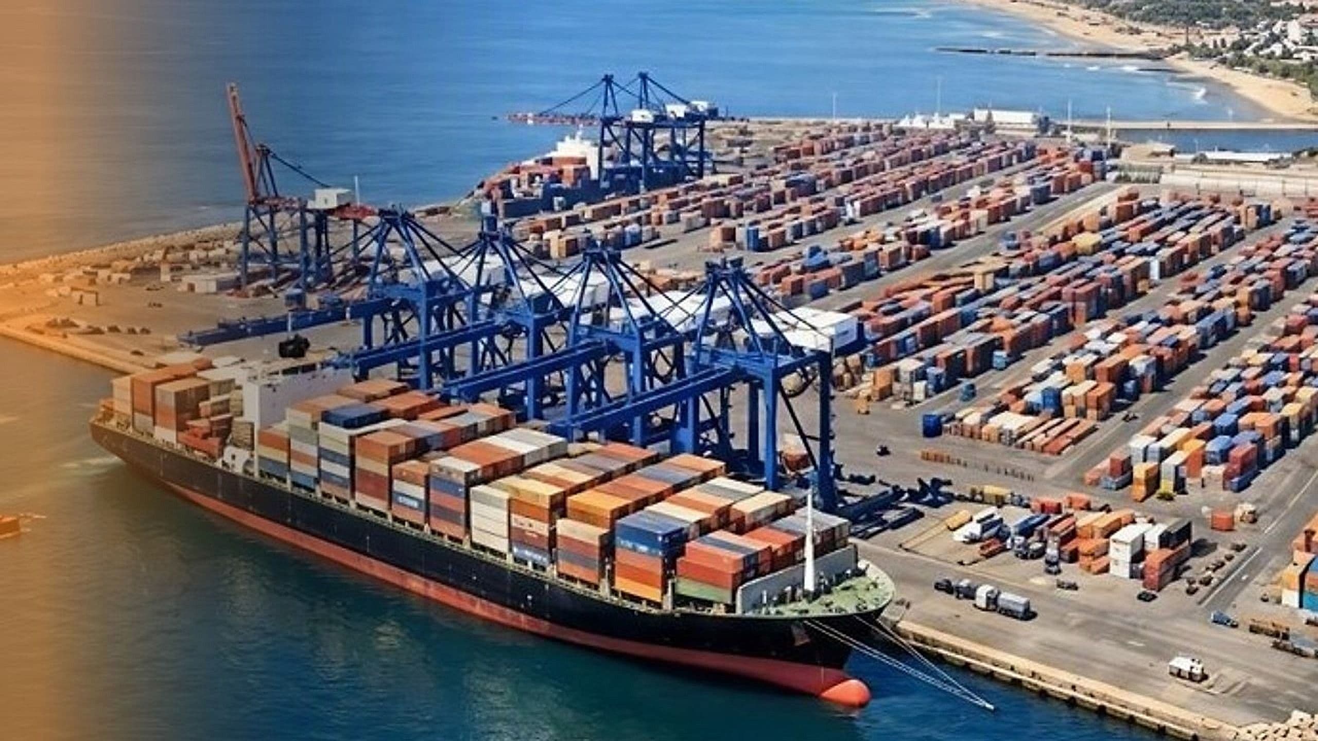 Aerial view of a container shipping port with gantry cranes, stacked containers and a docked cargo ship