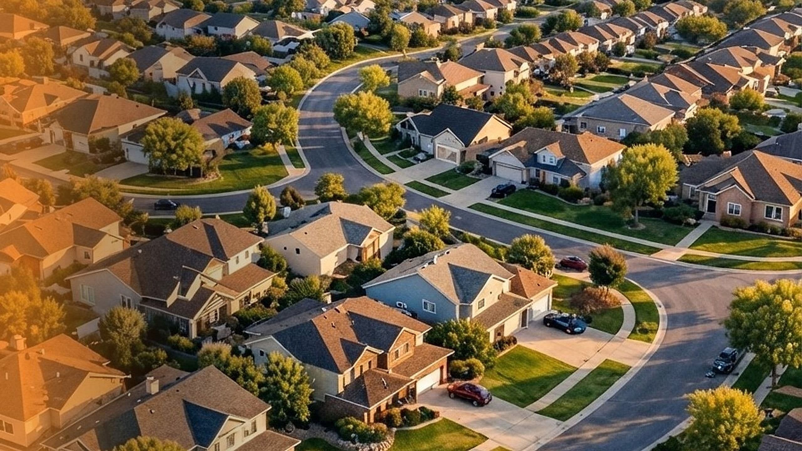Golden-hour aerial view of a suburban residential neighborhood with houses, driveways and curving streets