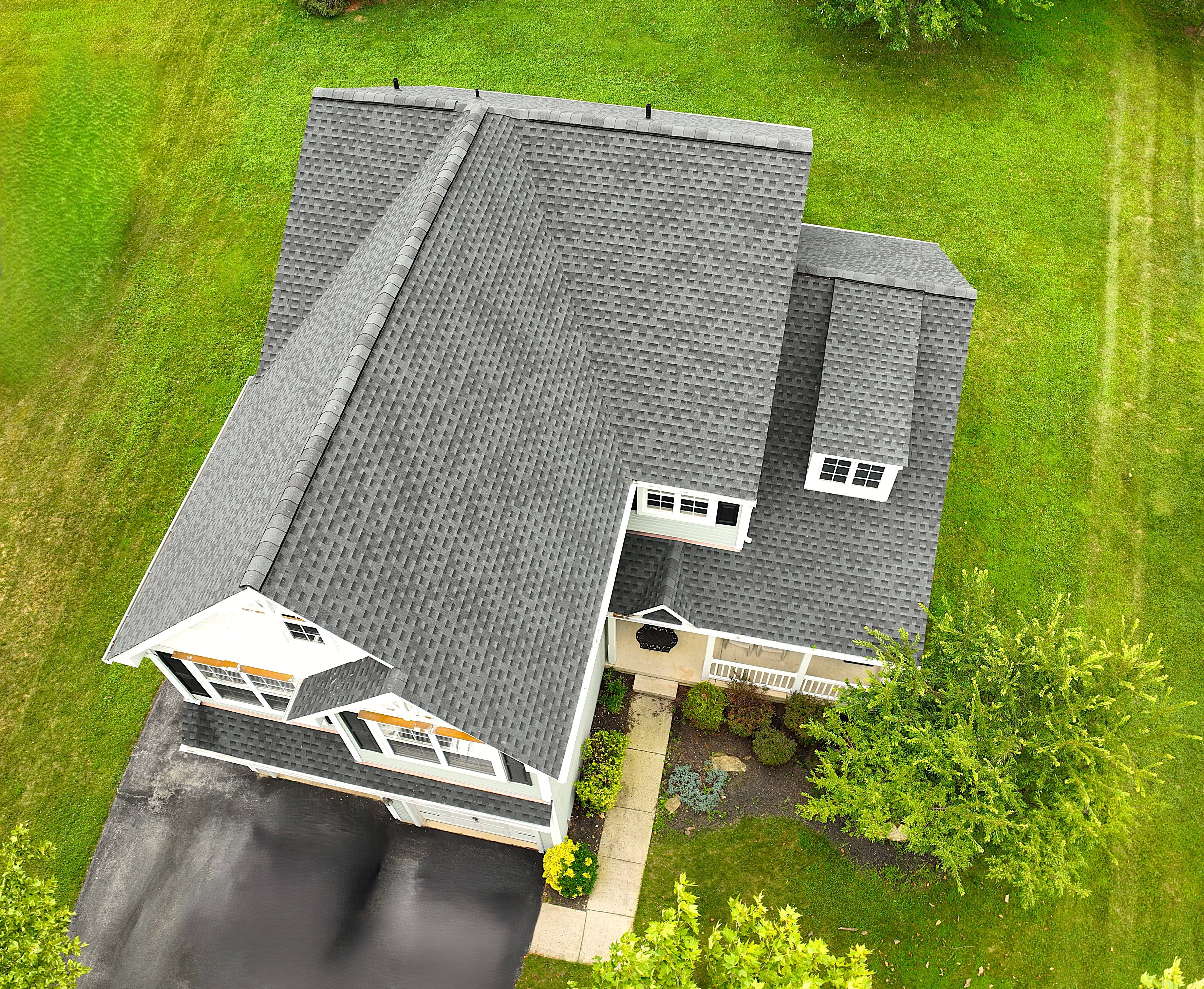 Aerial view of residential house with gray shingle roof surrounded by lush green landscaping showcasing professional drone real estate photography services